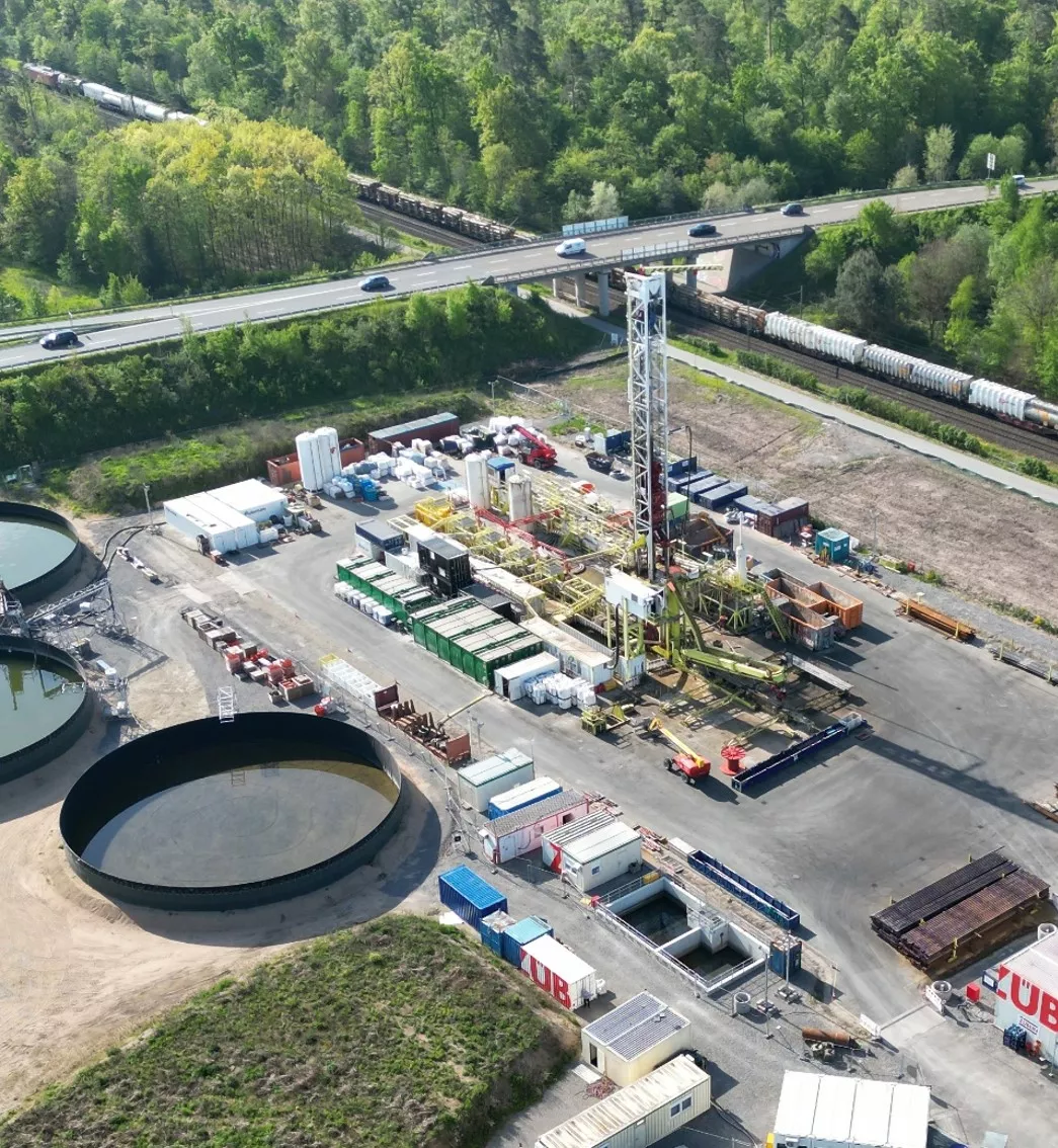 Foto zeigt ein Luftbild der tiefen Erdwärmebohrung in Graben-Neudorf mit einem Bohrturm, Baugeräten und großen, runden Wasserbecken