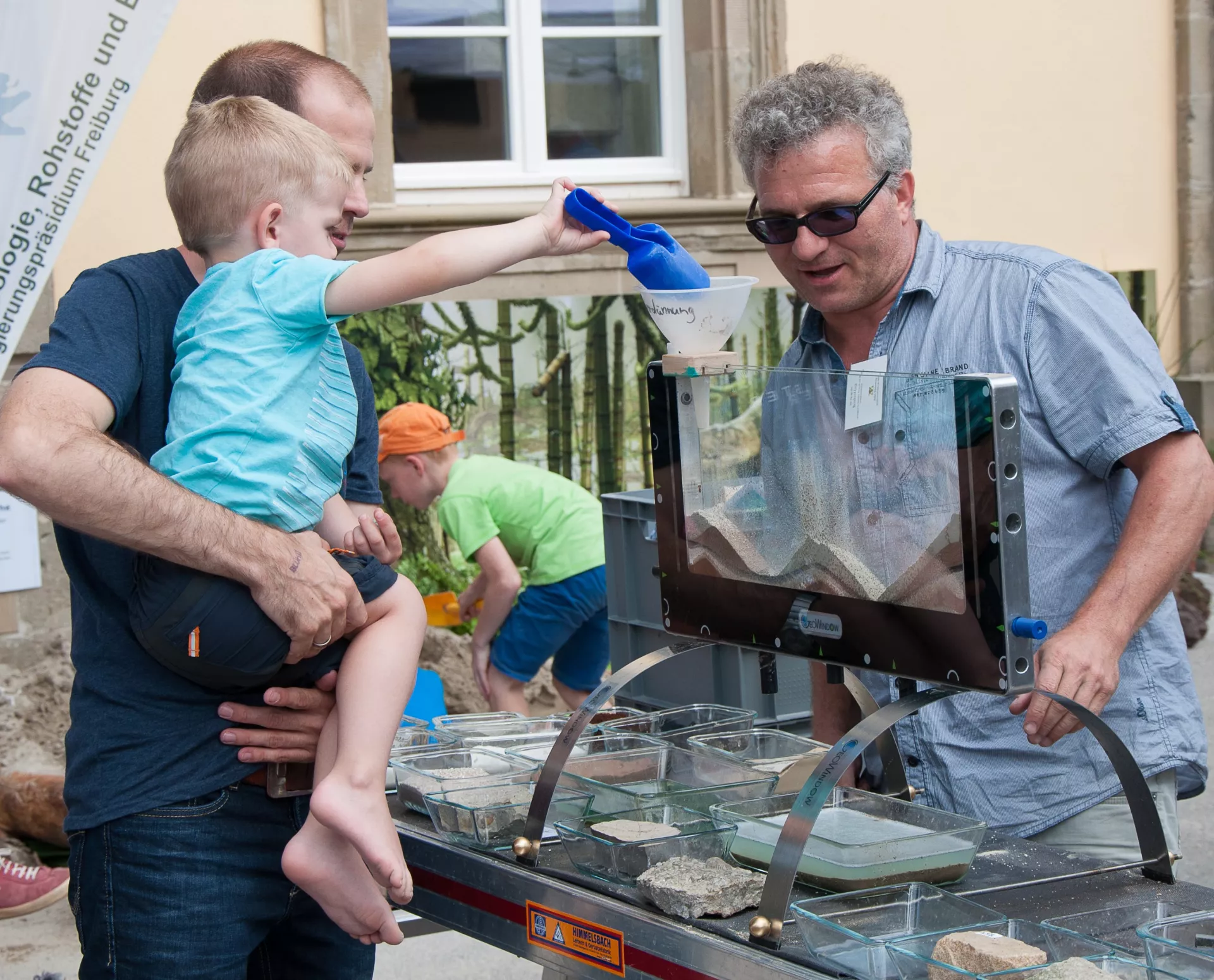 Ein Kind modelliert mit seinem Vater mit Hilfe des Geowindows spielerisch geologische Prozesse nach.