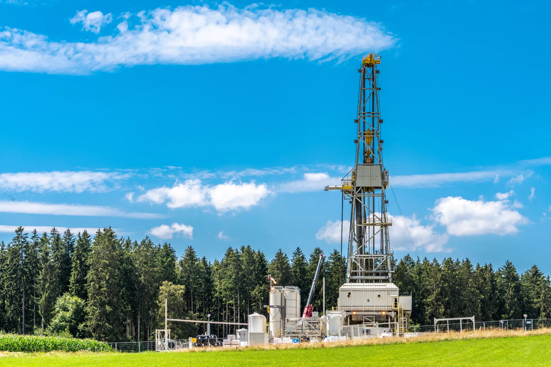 Foto zeigt Geothermie-Anlage mit Bohrturm vor einem Wald und blauem Himmel