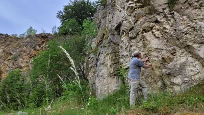 Ein Geologe steht mit Hammer Hammer in der Hand an einem Gesteinsaufschluss und nimmt Proben