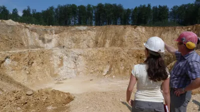 Zwei Personen stehen rechts der Bildmitte in einem Steinbruch. Die rechte Person zeigt auf den gegenüberliegenden Abbau.