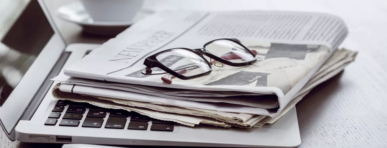Laptop mit Zeitung und Brille; im Hintergrund eine Kaffeetasse