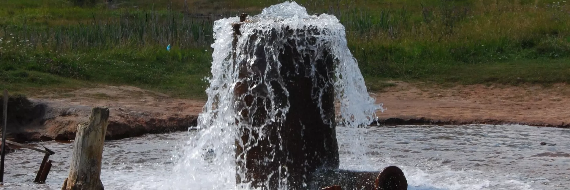 Artesisch, d. h. frei an der Erdoberfläche auslaufendes Grundwasser Foto zeigt ein dickes Rohr, das aus dem Erdboden ragt, aus dem Wasser mit Druck ausströmt