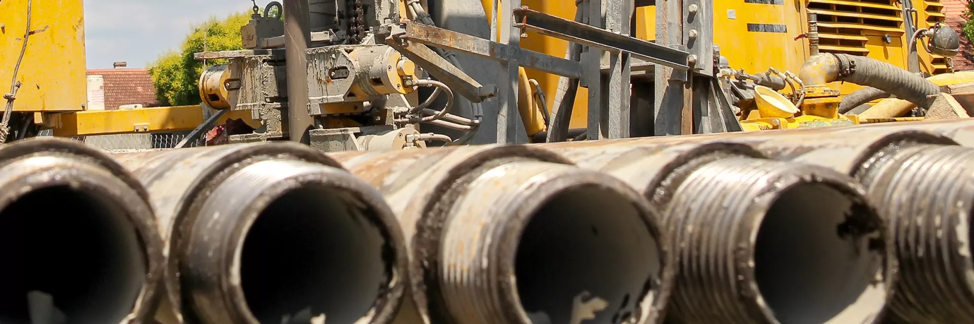 Foto zeigt im Vordergrund Metallrohre, im Hintergrund ein gelbes Bohrgerät