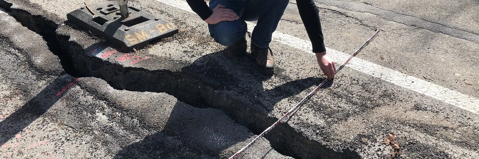 Ein Mann kniet an einem Längsriss einer Straße und misst mit einem Meterstab dessen Breite
